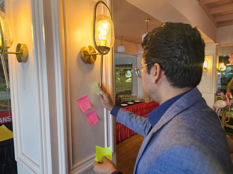 Harshadewa Amaratunga adding reflection notes to a wall of sticky notes